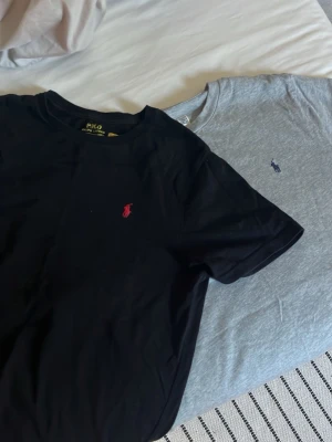 Två Polo Ralph Lauren t-shirts - Säljer två klassiska t-shirts från Polo Ralph Lauren för 299, en svart med röd logga och en grå med marinblå logga. 