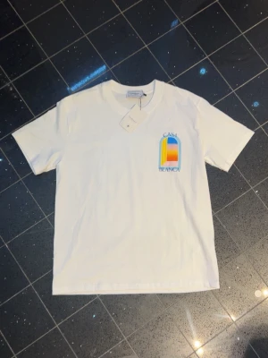 Vit CasaBlanca t-shirt med tryck - Säljer en fräsch vit t-shirt från CasaBlanca med färgglatt tryck på bröstet. T-shirten har korta ärmar, rund hals och är gjord i mjuk bomull. Perfekt för dig som gillar stilrena plagg med en twist.