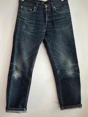 APC selvage jeans - Jeans i 100% bomull från märket APC i storlek 29.  Jeansen har ett litet hål vid knät som enkelt går att laga.  Utsida till midja: 89 cm Lår: 28 cm Knä: 20 Insida till gren: 67 cm Kontakta mig vid frågor, jag svarar så fort jag kan.