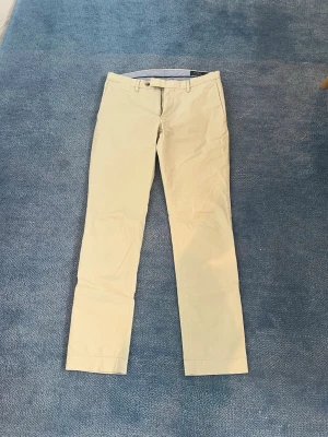 Beige chinos med slim/ raka - Snygga beige chinos med raka ben och klassisk passform. Byxorna har bälteshällor, knappgylf och två fickor fram samt två bakfickor med knapp. Perfekta för en clean och stilren look. Materialet känns mjukt och lätt,  bomull är matrialet
