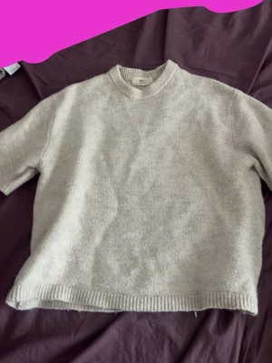 Beige stickad tröja från Gina Tricot - Mysig stickad tröja i beige från Gina Tricot, tillverkad i ullblandning. Tröjan har korta ärmar, rund halsringning och ribbstickade detaljer vid hals, ärmslut och nederkant. Perfekt för lager-på-lager och en chill look. Storlek XS men är väldigt baggy, passar nog S.