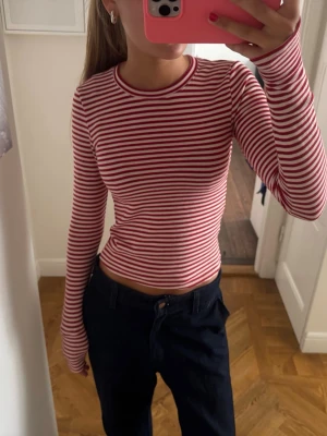 Rödvit randig långärmad topp - Säljer en långärmad topp med röda och vita ränder. Modellen är figurnära med rund halsringning och stretchigt material, perfekt för en avslappnad men ändå snygg look. Passar till både jeans och kjol.
