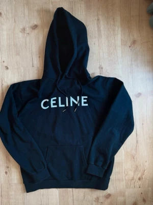 Svart hoodie  - Snygg svart hoodie med stor vit logga på bröstet och klassisk huva med dragsko. Hoodien har en stor magficka och ribbade muddar vid ärmar och nederkant. Perfekt för en chill och trendig look.