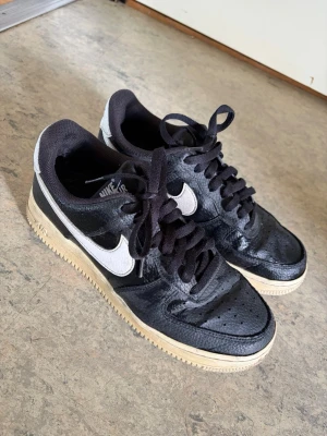 Nike Air Force 1 – Svart/Vit – Storlek 40,5 - Säljer ett par Nike Air Force 1 i färgen svart/vit, storlek 40,5. Skorna är använda men i bra skick – normala bruksspår men inget som påverkar användning eller stil.  ✔️ Storlek 40,5 ✔️ Färg: Svart/Vit ✔️ Bekväma och klassiska sneakers ✔️ Passar både vardag och streetwear.