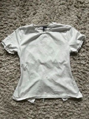 Vit t-shirt med snörning bak - Säljer en vit t-shirt från H&M i mjuk bomull. T-shirten har korta ärmar och en unik detalj med öppen rygg och snörning baktill. Perfekt för dig som vill ha en enkel men ändå speciell look. Passformen är normal och materialet känns skönt mot huden.