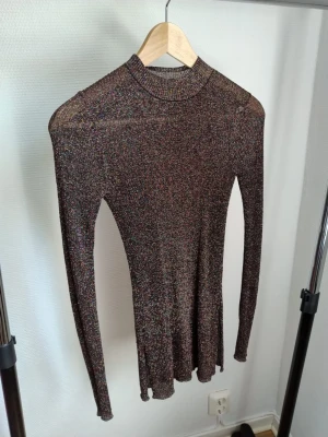 Fyra trendiga långärmade toppar - Säljer två snygga långärmade toppar. Ena är glittrig i mörka toner med figurnära passform och hög hals. Den andra är svart med transparenta meshärmar och volang vid ärmslut, också med hög hals. Perfekta för att lyfta din outfit!