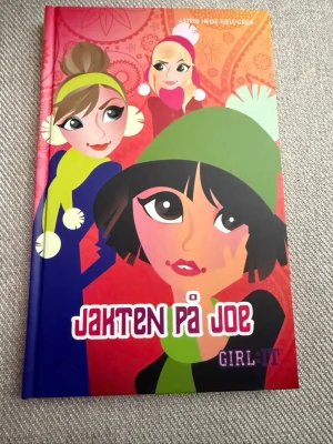 Jakten på Joe - Astrid Heise-Fjeldgren - En färgstark ungdomsroman med hårda pärmar, illustrerad framsida i rött, blått och grönt. Boken handlar om vänskap, kärlek och drömmar, och är en del av serien Kyss och Kanel. Perfekt för dig som gillar lättlästa och roliga berättelser om tonårsliv.