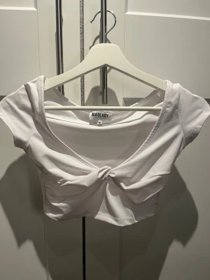 Vit croppad topp från Madlady - En vit croppad topp från Madlady med knyt framtill. Toppen har korta ärmar och en djupare ringning som ger en snygg och trendig look. Perfekt att matcha med höga jeans eller kjol för en fräsch stil.