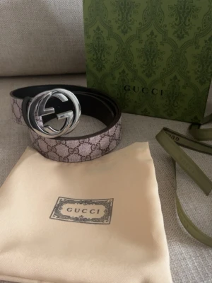  GG Supreme bälte med silverdetalj - Säljer ett GG Supreme bälte med klassiskt monogrammönster i beige och brunt. Bältet har en stor, rund silvrig GG-logga som spänne och är tillverkat i skinn med canvasöverdrag. Perfekt accessoar för att lyfta vilken outfit som helst.