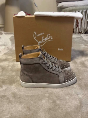 Gråa Christian Louboutin spikes sneakers - PRIS KAN SÅKLART DISKUTERAS‼️‼️.           Snygga gråa high top sneakers från Christian Louboutin i mocka med silverfärgade nitar på tån. Skorna har vita sulor, gråa skosnören och en lyxig känsla. Perfekta för dig som vill sticka ut med en edgy och exklusiv stil.  