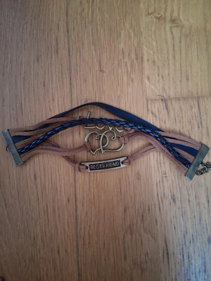 Brunt och svart armband med text - Unikt armband med flera band i brunt och svart konstläder, dekorerat med en metallbricka med texten 'BEST FRIEND' och ett metallhjärta med infinity-symbol. Perfekt accessoar för att visa uppskattning till en vän.