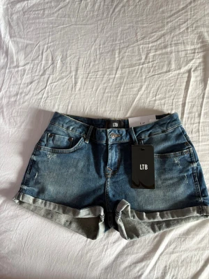 Helt nya LTB low waist, slim short jeansshorts - Säljer ett par klassiska blå jeansshorts från LTB med uppvikta benslut och femficksmodell. Shortsen har låg midja och stängs med knapp och dragkedja. Perfekta till sommaren och lätta att matcha med allt.
