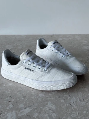 Adidas 3MC Vulc White | EU 38 2/3  - Fräscha vita sneakers från Adidas med klassisk låg profil och diskret logga på sidan. Skorna har ovandel i canvas, vita snören och sula i gummi. Perfekta för en clean och stilren look. Passar till det mesta och är riktigt lätta på foten.
