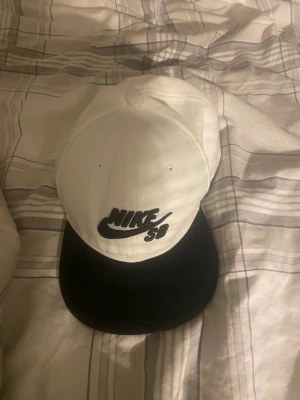 Nike SB svartvit keps - Snygg svartvit keps från Nike SB med klassisk logga broderad framtill. Kepsen har en rak skärm i svart och själva kronan är vit. Tillverkad i bomullsmix och har justerbar passform. Perfekt för en streetwear-look.