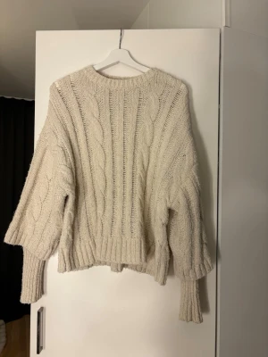 Beige kabelstickad tröja från Zara - Mysig beige kabelstickad tröja från Zara med breda ärmar och ribbade muddar. Tröjan har en avslappnad passform och rund halsringning. Perfekt för lager på lager och ger en trendig oversized look.