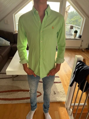 Grön skjorta från Ralph Lauren - Säljer en ljusgrön skjorta från Ralph Lauren med klassisk button-down krage och broderad logga på bröstet. Skjortan har långa ärmar, knappar framtill och är tillverkad i bomull. Perfekt för en avslappnad men ändå stilren look.