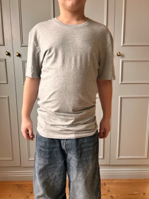 Grå t-shirt från Polo Ralph Lauren - Snygg grå t-shirt från Polo Ralph Lauren med klassisk rund hals och korta ärmar. Tillverkad i mjuk bomull och har den ikoniska svarta Polo-loggan broderad nedtill. Perfekt basplagg för en avslappnad stil.
