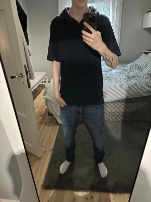 Mörkblå piké från essential clothing  - Säljer en mörkblå piké med klassisk krage och korta ärmar. Toppen har en enkel och stilren design, perfekt för dig som gillar en clean look. Materialet är ett så kallat ”handduks-material” som känns mjukt och bekvämt mot huden.