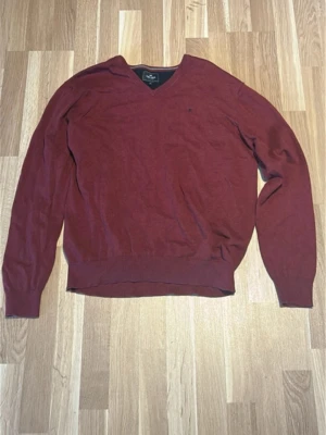 Vinröd stickad tröja Ralph Lauren - Vinröd stickad tröja från Ralph Lauren med diskret broderad logga på bröstet. Tröjan har V-ringning, långa ärmar och ribbade muddar vid ärmslut och nederkant. Perfekt för lager på lager och klassisk stil. Materialet känns mjukt och följsamt.
