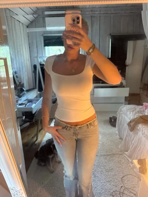 Vit topp med kort ärm - Säljer en vit topp med korta ärmar och fyrkantig ringning. Toppen har en tight passform och är tillverkad i ett stretchigt bomullsmaterial som sitter snyggt på kroppen. Perfekt att styla med jeans eller kjol.
