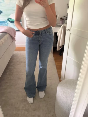 Blå bootcut jeans - Säljer ett par ljusblå bootcut jeans med medelhög midja och klassisk femficksdesign. Jeansen har en snygg utsvängd passform från knät och är tillverkade i ett mjukt denimtyg. Perfekta för en trendig och avslappnad look.