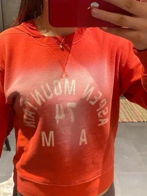 Röd sweatshirt Aspen Mountain - Jätte fin röd sweatshirt med trycket 'Aspen Mountain 74 AM' i vitt framtill. Tröjan har rund halsringning och ribbade muddar vid ärmslut och nederkant. För mej som är 170 är den lite kort i magen men ingen som ör alldeles för stort problem. Säljer på grund av att jag helt enkelt inte tycker om den längre.