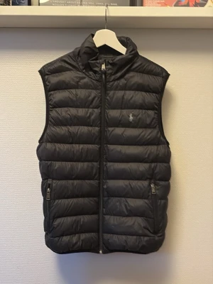 Svart dunväst från Polo Ralph Lauren - Säljer en riktigt fet svart Polo-Ralph-Lauren väst. Västen är väl använd men fortfarande i nyskick utan synliga defekter, perfekt till våren och svala sommardagar. Pris 950 men kan sänkas vid snabb affär!