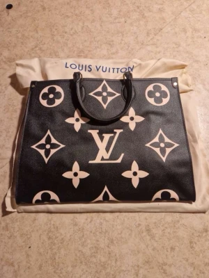 Svart Louis Vuitton Monogram Tote - Stilren svart handväska från Louis Vuitton med ikoniskt monogrammönster i beige. Väskan har två handtag och är tillverkad i tåligt läder. Perfekt för dig som vill ha en lyxig och rymlig tote med klassisk design och stora LV-detaljer.
