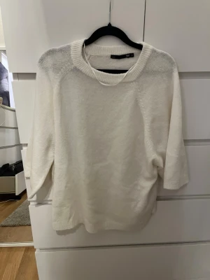 Vit stickad tröja från Lager 157 - Mysig vit stickad tröja från Lager med rund halsringning och trekvartsärmar. Tröjan har en avslappnad passform och är tillverkad i ett mjukt, fluffigt material som känns skönt mot huden. Perfekt för lager på lager och enkel att matcha.