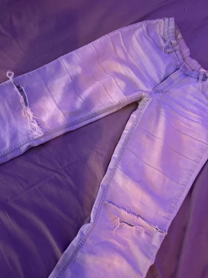 Ljusblå ripped flare jeans - Säljer ett par ljusblå jeans med utsvängda ben och slitna detaljer vid knäna. Jeansen har klassisk femficksdesign och är tillverkade i denim. Perfekta för en avslappnad och trendig look. Stretchiga 