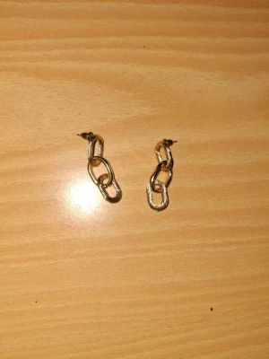 Chunky guldörhängen i kedjedesign - Säljer ett par chunky örhängen i guld med cool kedjedesign. Perfekta för dig som vill ha ett statement-smycke som sticker ut. Örhängena har en modern och trendig look med tre sammanlänkade länkar. Passar till alla tillfällen!