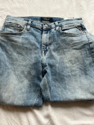 Ljusblå jeans från Replay - Säljer ett par ljusblå jeans från Replay med klassisk femficksmodell och snygg tvättad look. Jeansen har raka ben och detaljerade sömmar på bakfickan. Perfekta för en avslappnad och trendig stil.