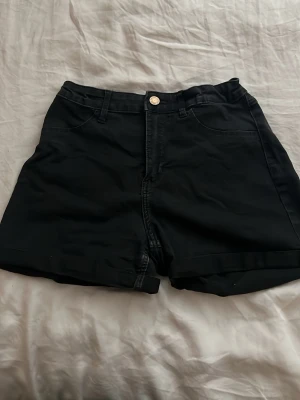 Svarta mid rise shorts - Snygga svarta shorts med stretchade material och klassisk femficksdesign. De har knapp och dragkedja framtill samt uppvikta benslut. Perfekta till sommaren och lätta att matcha med olika stilar.