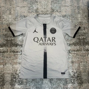 PSG x Jordan grå matchtröja - Snygg grå PSG matchtröja i samarbete med Jordan. Tröjan har svart vertikal rand på framsidan, PSG-logga och Jordan-logga på bröstet samt Qatar Airways-tryck. Svarta detaljer vid ärmslut och sportig passform i lätt funktionsmaterial.