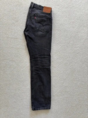  Levi's Jeans 501 Gråsvarta - Jag säljer nu ett par gråsvarta Levis 501 jeans i storleken 32 32. Byxorna är använda men det finns inge synliga defekter, små synliga kan vara knävecken men det kommer från normal användning. Jeansen har normal midja och är tillverkade i slitstark denim. 