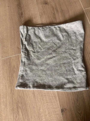 Grå tubtopp i bomull - En enkel och stilren grå tubtopp i mjukt bomullsmaterial. Perfekt att matcha med jeans eller kjol för en avslappnad look. Toppen är ärmlös och har en rak passform.