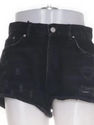 Svarta jeansshorts med rå kant - Säljer ett par svarta jeansshorts med och råa kanter. Shortsen har slitna detaljer, fem fickor och knappgylf. Perfekta för en avslappnad och trendig look. Mer som storlek 36 ( VILL BLI AV MED SNABBT)