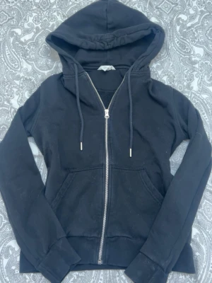 Svart zip hoodie från H&M XS - En svart hoodie från H&M i storlek XS med dragkedja framtill, huva med dragsko och två fickor. Tillverkad i mjukt bomullsmaterial som är skönt att ha på sig. Perfekt för en avslappnad och chill stil.