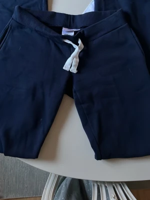 Ultra low waist byxor Gina Tricot - Mörkblå mjukisbyxor från Gina Tricot med ribbad midja och vita dragsnören. Byxorna har en klassisk, avslappnad passform och är tillverkade i mjukt material som känns skönt mot huden. Perfekta för chill dagar eller när du vill vara bekväm.