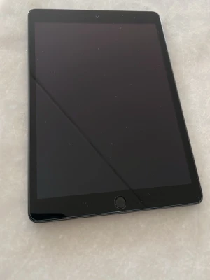 Apple iPad med svart skärm - Säljer en stilren Apple iPad i färgen space gray med svart framsida och rund hemknapp. Baksidan har den klassiska Apple-loggan och en gul etikett längst ner. Surfplattan har en slimmad design och är tillverkad i aluminium. Skal till ipaden ingår även skärmskydd.