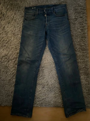 Faded G-STAR jeans - Säljer ett par mörkblå jeans med rak passform och klassisk femficksdesign. Jeansen har subtila slitningar och är tillverkade i denim. Perfekta för en avslappnad och stilren look.