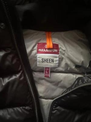 Svart dunjacka Parajumpers Sheen L - Snygg svart dunjacka från Parajumpers, modell Sheen. Jackan har huva, gul detalj vid dragkedjan och klassisk PJS-logga på ärmen. Puffig design med breda kanaler och dragkedja framtill. Perfekt för kalla vinterdagar. Använd i bara 3veckor, köpt för 7700kr