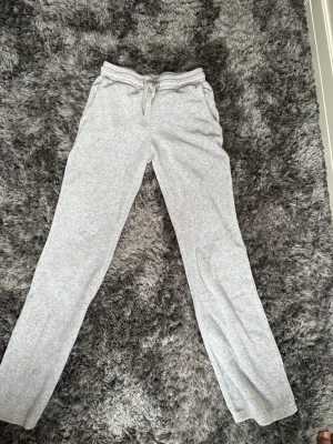 Två par mjukisbyxor i grått och svart - Säljer två par mjukisbyxor, ett par i ljusgrå bomull med dragsko och fickor, samt ett par i svart velour med bred resår i midjan och avslappnad passform. Perfekta för chill dagar hemma eller när du vill vara extra bekväm.