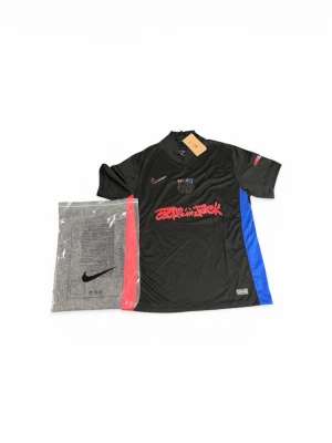 FC Barcelona fotbollströja  -  *   Produkt: Cactus Jack x FC Barcelona fotbollströja ⚽ *   Märke: Nike *   Design: Svart med röd och blå detaljer, Cactus Jack-logotyp. *   Detaljer: Ny med taggar och förpackning. *   Storlek: Medium (M) 📏 *   Material: Tyg verkar vara polyester. *   Stil: Perfekt för både fotbollsfans och trendmedvetna. En riktig samlarobjekt!  Hashtags: #CactusJack #FCBarcelona #Nike #FootballJersey #Medium #LimitedEdition #Streetwear #ForSale 💯