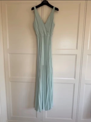Dagmar långklänning mintgrön S - Säljer en elegant ljusgrön/mintgrön långklänning från Dagmar. Klänningen har v-ringning, plisserad design och är ärmlös. Perfekt för sommarens speciella tillfällen. Luftigt material som ger ett snyggt fall. Använd på ett bröllop en gång. Kostade ca 4500kr ny