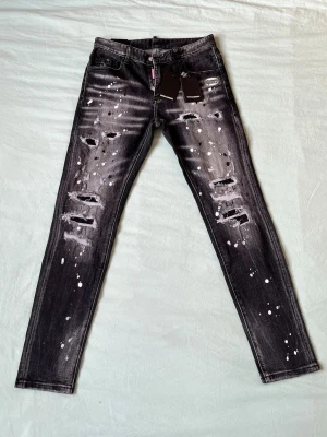Svarta distressed jeans Dsquared2 - Säljer ett par svarta skinny jeans från Dsquared2 med slitningar, hål och vita färgstänk för en riktigt edgy look. Jeansen har klassisk femficksmodell och logotypdetaljer vid fickan. Perfekta för dig som gillar streetwear och statement-plagg.