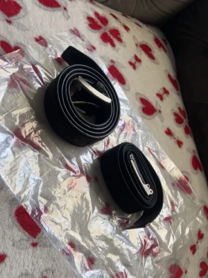 Två svarta bälten med metallspänne - Säljer två stilrena svarta bälten. Ett i mocka med klassiskt metallspänne och ett i textil med silverfärgat spänne där det står PX. Perfekta accessoarer för att lyfta din outfit.