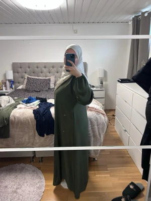 Olivgrön abaya med stängda ärmar - Snygg olivgrön abaya med lös passform och stängda ärmar. Klänningen har en enkel och stilren design utan mönster, perfekt för dig som gillar minimalistiskt mode. Tillverkad i ett mjukt och lätt material som faller fint. Från luude collection