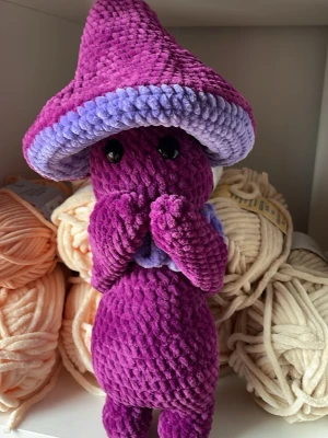 Lila virkad Mushroom guy  - En handgjord, virkad Mushroom guy i mjukt lila och ljust lila garn. Figuren har stora svarta säkerhetsögon och en stor svamphatt. Perfekt som present till någon som gillar unika mjukisdjur.