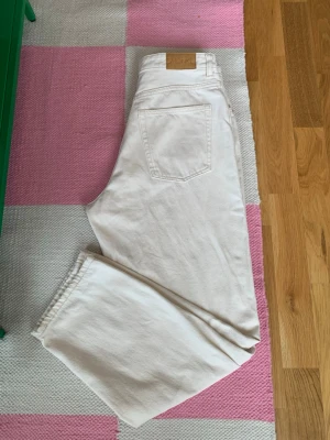 Vita raka jeans från Monki - Säljer ett par vita jeans från Monki med rak passform och klassisk femficksdesign. Jeansen har hög midja och är tillverkade i ett kraftigare bomullstyg. Perfekta för en clean och stilren look.